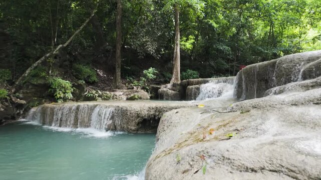 Tiered rock ledges carry small cascades into a turquoise jungle pool under dense green canopy in Erawan National Park.