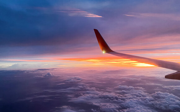 Airplane wing view of beautiful sunset sky background with bright golden light and soft purple clouds for panoramic travel design