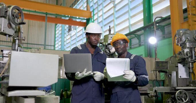 two african adult male engineers study laptop and document near machinery, compare production detail in workshop, digital monitoring, safety teamwork and workflow planning