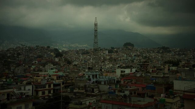 Electricity pylon rises above dense Kathmandu rooftops under stormy sky