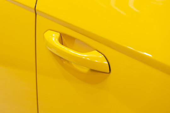 Close up of yellow car door handle and sleek automotive bodywork. Professional vehicle photography showcasing vibrant paint finish and modern transport design. Clean minimalist aesthetic