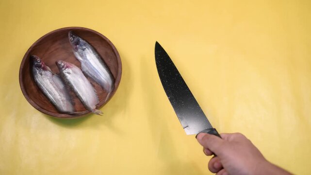 Close-up 4K video of a fresh raw Ompok bimaculatus (Pabda/Parda fish) in a wooden bowl held by an Indian man against a yellow background. Seafood, aquaculture, nutrition, and fresh market concepts.