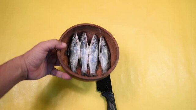 Close-up 4K video of a fresh raw Ompok bimaculatus (Pabda/Parda fish) in a wooden bowl held by an Indian man against a yellow background. Seafood, aquaculture, nutrition, and fresh market concepts.