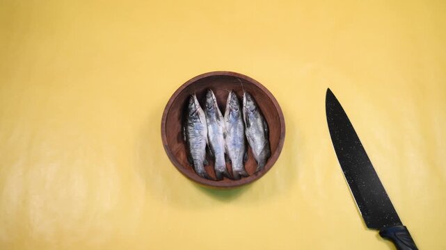 Close-up 4K video of a fresh raw Ompok bimaculatus (Pabda/Parda fish) in a wooden bowl held by an Indian man against a yellow background. Seafood, aquaculture, nutrition, and fresh market concepts.