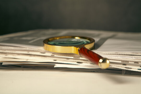 Magnifying glass and pile of newspapers on black background, closeup