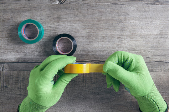 Hands in green protective gloves holding electrical tape