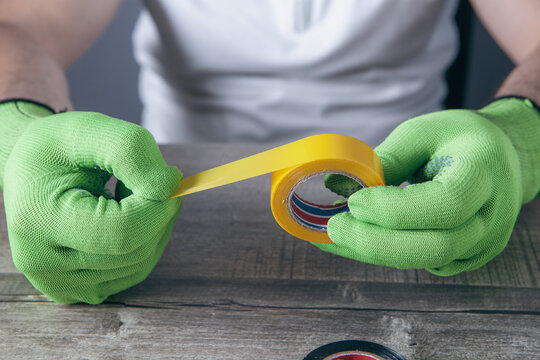 Hands in green protective gloves holding electrical tape