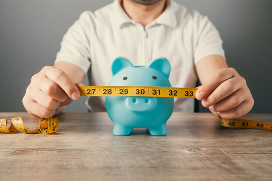 Man's hands holding a  piggy bank with a measuring tape on a wooden background