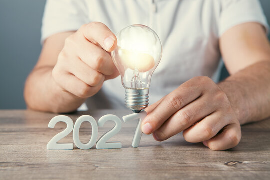 Hand holding a light bulb with the word 2027 on a wooden background