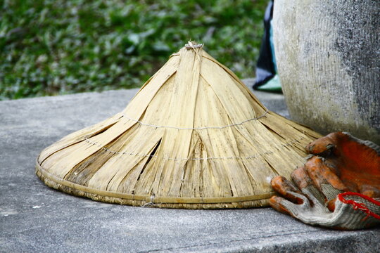 Traditional Asian conical straw hat and working gloves on concrete.
