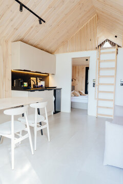 Vertical shot of bright wooden tiny house interior with loft ladder, kitchenette and bedroom