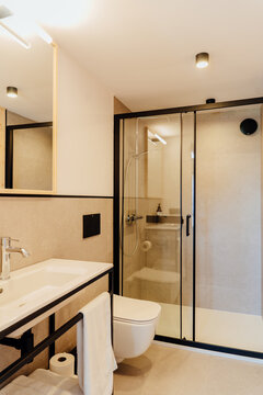 Vertical shot of elegant bathroom with glass shower, white sink and black fixtures
