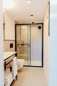 Vertical shot of modern bathroom with glass shower, sink, towels and warm lighting
