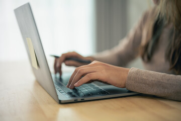 Fototapeta premium Close-up of a person typing on a laptop computer at a desk in a modern office space with natural light