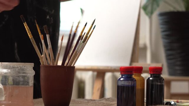 Close-up of man artist hand choosing and picking oil paint brushes in his workshop