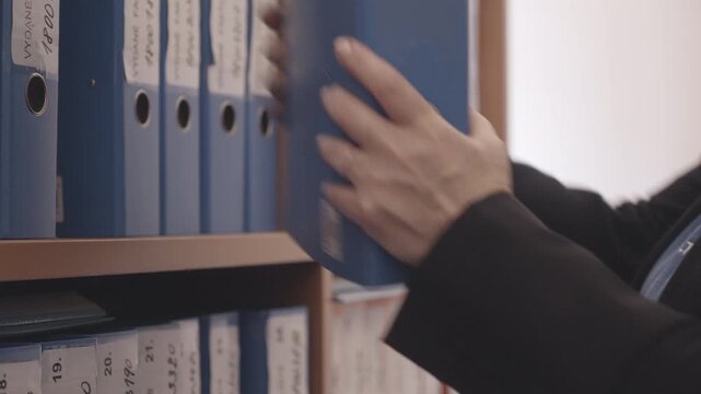 Close side view of an office administrator replacing a binder after reviewing documents, highlighting organized record keeping and efficient office workflow.