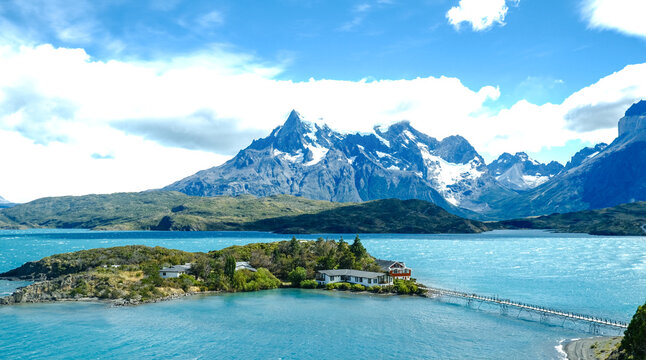 A small island with a red house surrounded by turquoise waters, with the dramatic peaks of Torres del Paine rising in the background, Patagonia, Chile