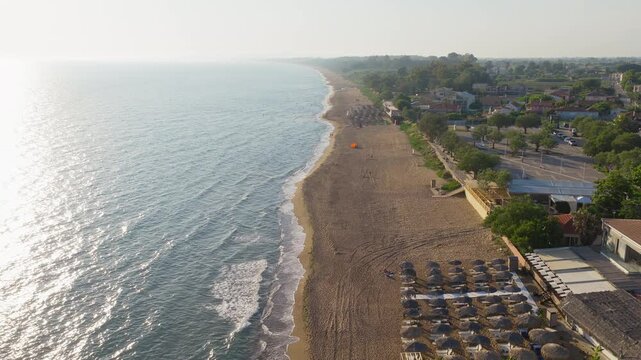 Aerial panorama of Kourouta Beach coastline with organized umbrellas and calm sea, establishing dolly at sunrise, serene backdrop