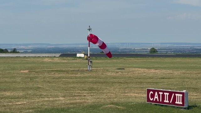 A view of a windsock on a grass field, near the runway. daylight