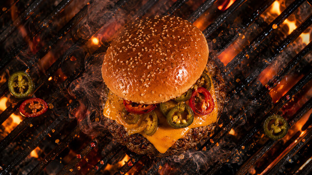 Delicious grilled hamburger with cheese and jalapenos, sizzling over an open flame, perfect for summer grilling.
