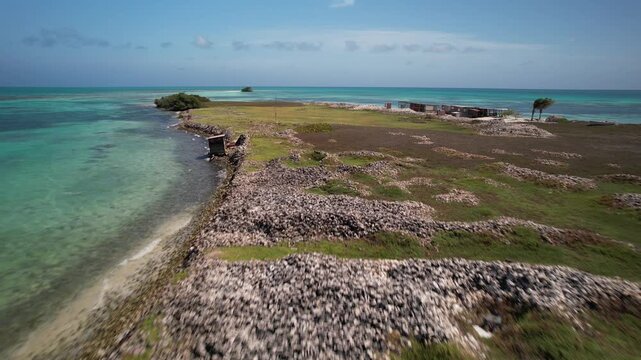Stunning drone perspective of a remote Caribbean island, highlighting the vivid contrast between white conch shells mountains, green grass and coral reefs.
