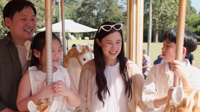 Happy Asian Family Riding Carousel Together During Sunny Outdoor Vacation