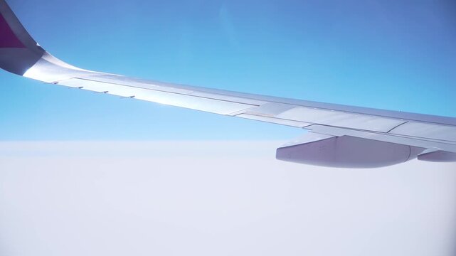 Airplane flying above clouds with extended wing and visible flap sections from passenger window view. Close perspective emphasizing panel lines, joints and aerodynamic surface. Aviation engineering