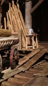 A wooden cart stands in a lumberyard surrounded by logs and planks. The scene shows the tools and materials used for woodworking in a working environment.