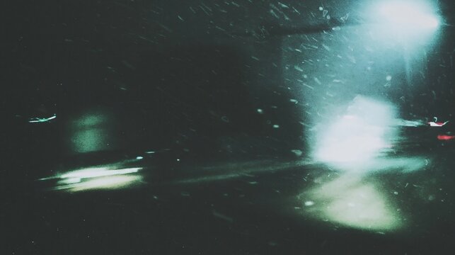Abstract blur of city lights and falling snow at night, creating a moody, atmospheric urban scene