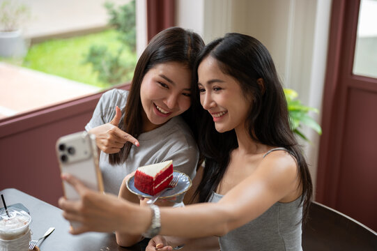 Asian women taking selfie together with red velvet cake during a cheerful cafe gathering with friend