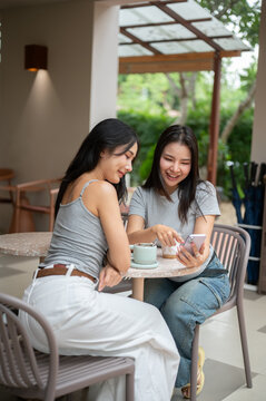 Beautiful Asian woman pointing finger at smartphone screen while talking with her friend at a cafe.