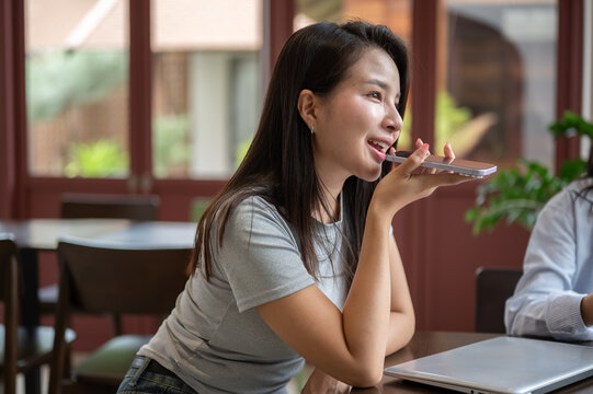 Young Asian woman recording a voice message with smartphone at workspace