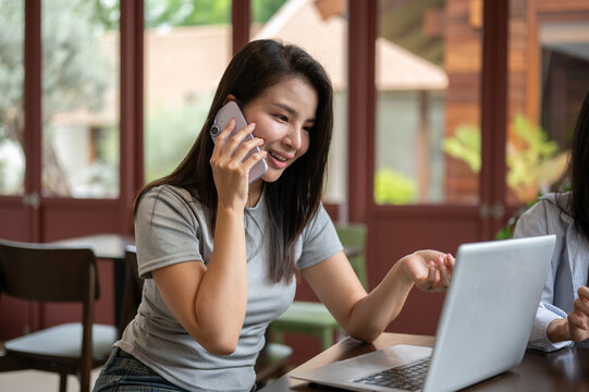 Asian woman freelancer making a phone call while using laptop during a work session in a modern cafe