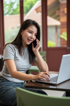 Young Asian woman talking on smartphone while working on laptop