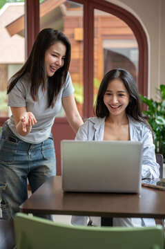Two young Asian women collaborating on laptop in modern workspace