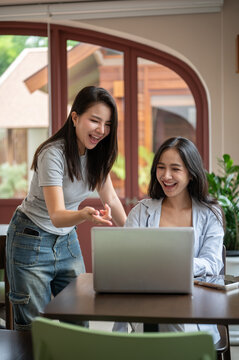 Asian female coworkers looking at a laptop while sharing ideas during a productive meeting in cafe.