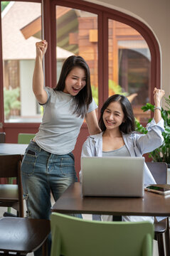 Two happy Asian businesswomen celebrating success with laptop