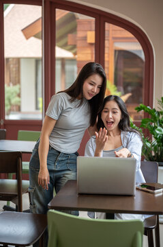 Two excited young Asian women reacting to good news on laptop