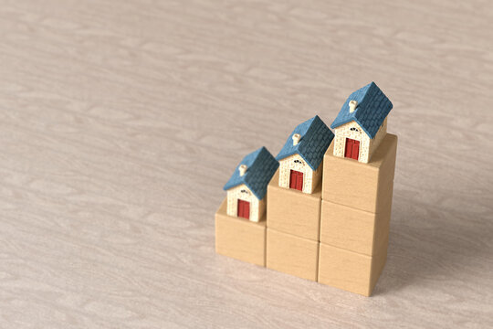 Small model houses sitting on ascending wooden block steps to represent rising home values and increasing real estate prices on a textured surface