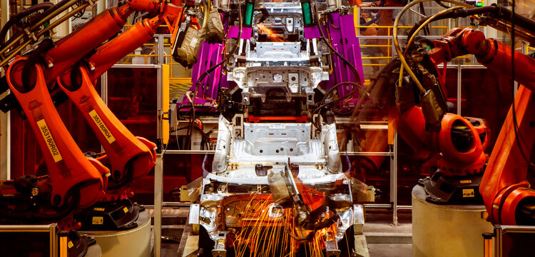 Automated robotic arms on a factory assembly line are welding car frames.