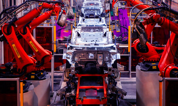 Automated robotic arms on a factory assembly line are welding car frames.