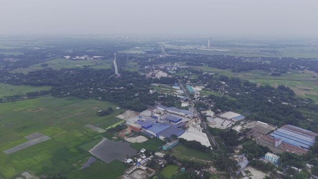 Cinematic aerial footage flying forward above a semi-urban area with homes, local businesses, cultivated farmland, and expansive open land. 