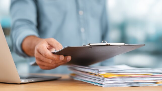 A man holds a tablet and documents. A middle-aged man in an office is working with papers and a tablet on a table.