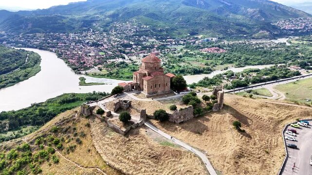 Stunning aerial perspective showing the historic jvari monastery, a masterpiece of early georgian christian architecture, standing on a rocky mountaintop overlooking the town of mtskheta