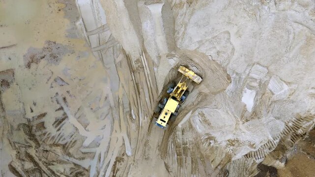 Aerial view of deep mining pit. Heavy machinery works in vast earth excavation. Trench walls show disturbed soil and rock. Ideal for industrial or construction projects