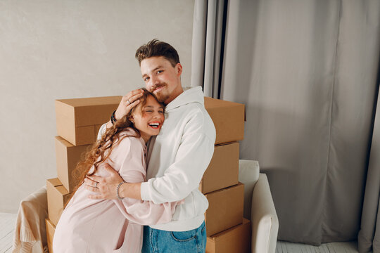 Happy young couple man and woman hugging after moving with cardboard boxes to new estate home apartment