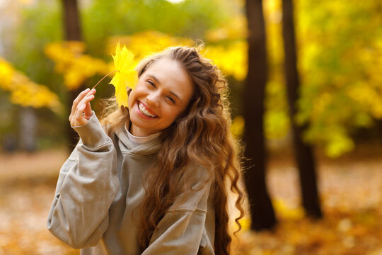 Young smiling lady holding yellow leaf in her hand in the park at sunset.