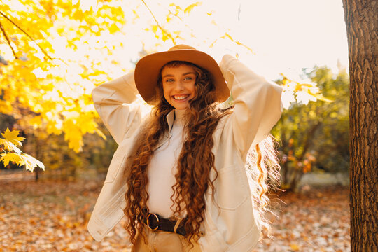 Smiling young woman portrait in the autumn public park with the yellow leaves with sunset rays.