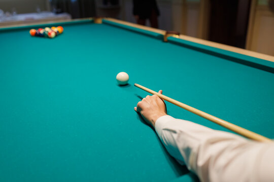 Billiard player hand holding cue plays snooker on pool table