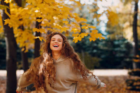 Smiling young woman with curly hairstyle enjoys the autumn weather in the park with the yellow leaves 